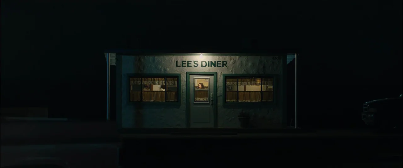 To Leslie (2022) movie still: wide — A small, weathered building with a sign reading Lee's Diner stands alone at night. Warm light spills through…