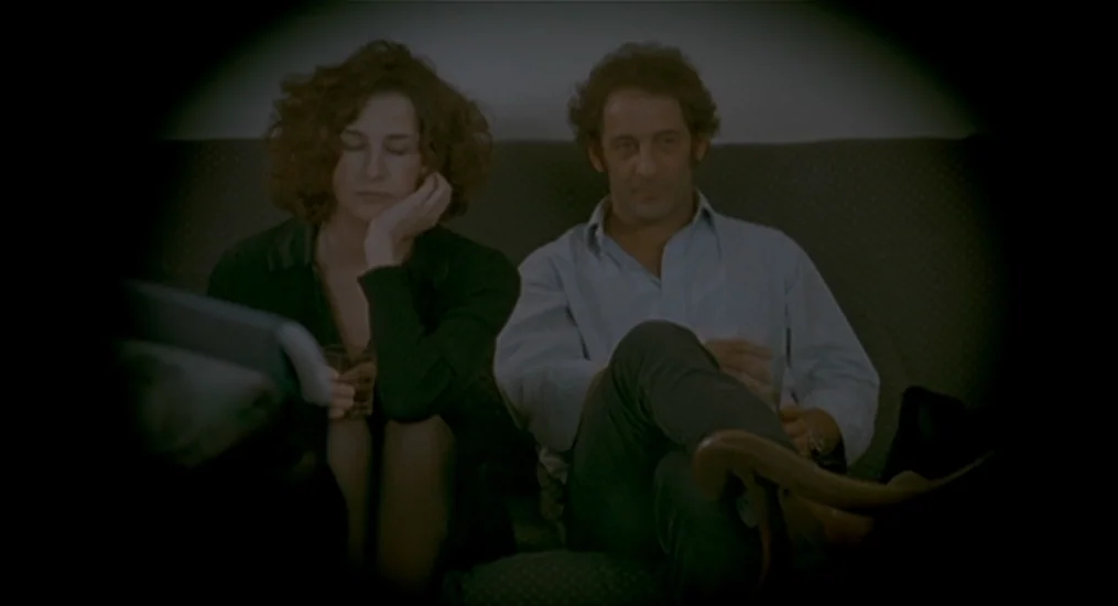 Vendredi Soir (2002) movie still: medium — A man and a woman sit together on a sofa in a dimly lit room. Both individuals are looking forward while…