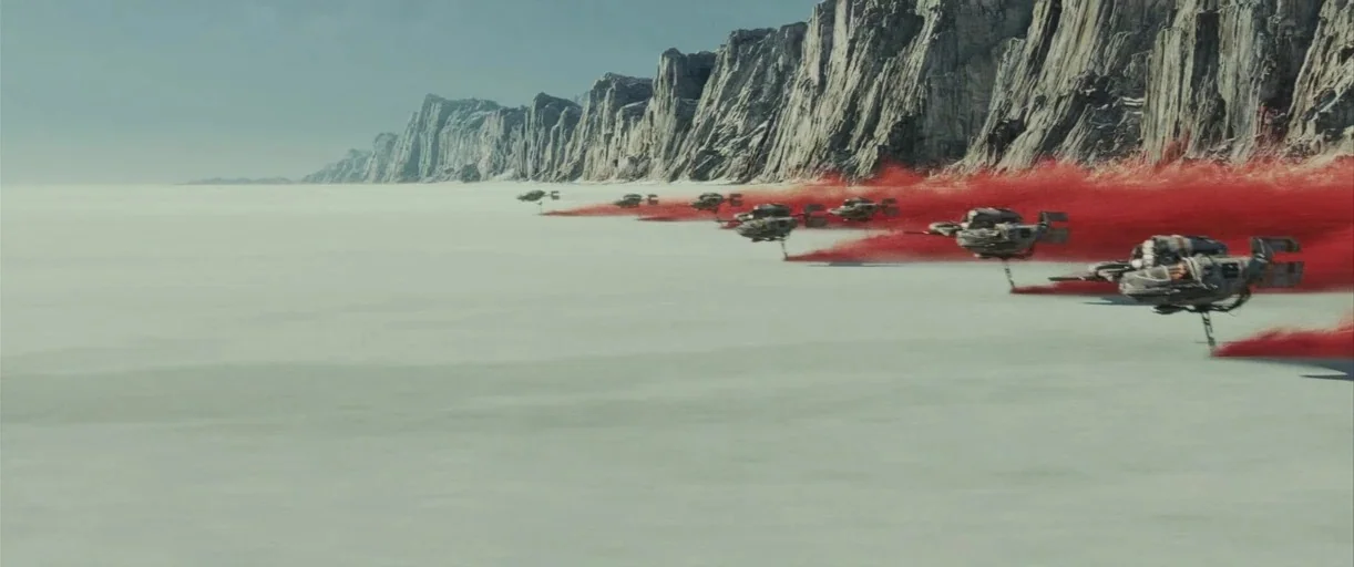 Star Wars: The Last Jedi (2017) movie still: wide — A vast, flat, pale white salt plain stretches toward a jagged rocky cliff formation. A group of…