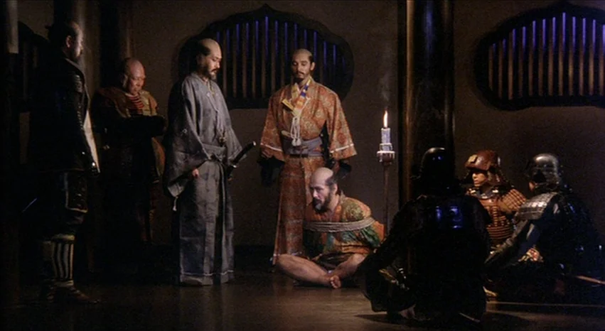 Kagemusha (1980) movie still: wide — A dark, wood-paneled room in a traditional Japanese structure features arched lattice windows. Several men in…