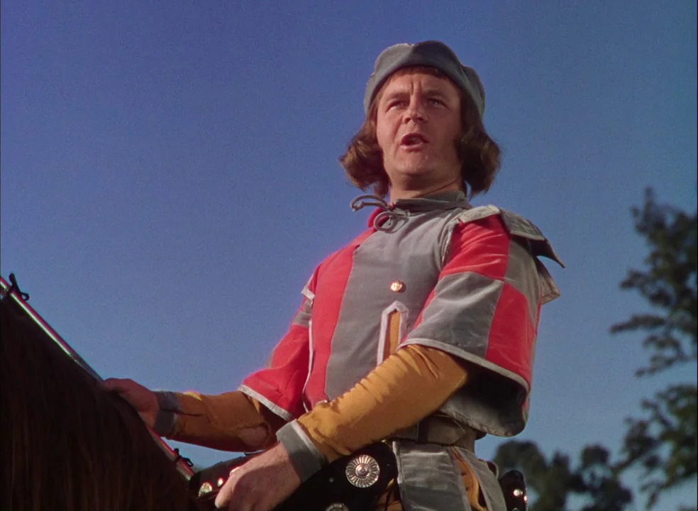 The Adventures of Robin Hood (1938) movie still: medium — A man in medieval attire rides a horse against a clear, solid blue sky. He wears a…