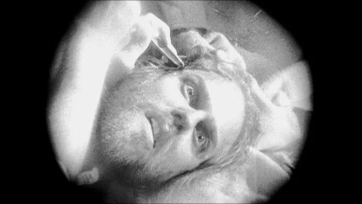 Dracula: Pages from a Virgin’s Diary (2002) movie still: closeup — A close-up view through a circular aperture shows a man lying down in darkness.…