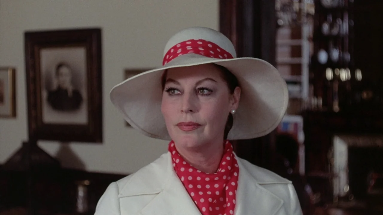 The Sentinel (1977) movie still: closeup — A well-lit room features a framed portrait hanging on a light-colored wall. A mature woman wearing a…