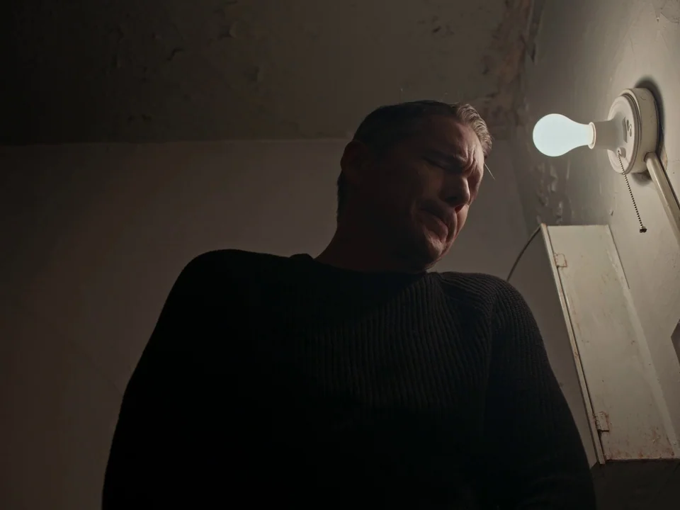 First Reformed (2017) movie still: medium — A stark utility space with peeling paint and a bare wall. A middle-aged man stands near an exposed…