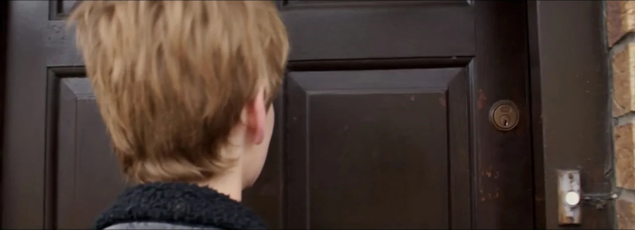 DannyBoy (2020) movie still: closeup — A close-up view of a person standing before a dark brown residential door. The person is seen from behind,…