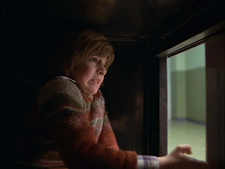 The Shining (1980) movie still: medium — A child hides inside a dark, cramped space looking out into a brightly-lit room. The child grips the edge…