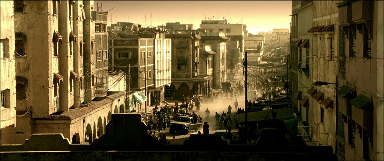 Black Hawk Down (2001) movie still: establishing — A dense city street is lined with weathered buildings featuring arches and hanging wires.…