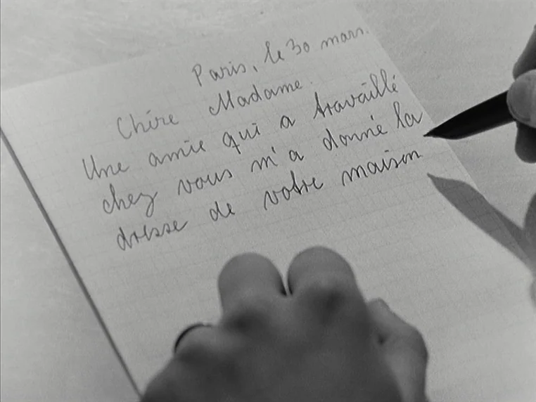 Vivre Sa Vie (1962) movie still: closeup — A piece of grid paper lies on a surface with French handwriting on it. A hand holds a black fountain pen…