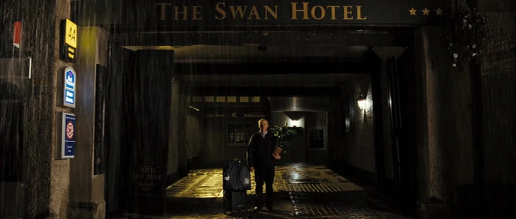 Hot Fuzz (2007) movie still: wide — The stone archway of a hotel entrance is visible at night during heavy rain. A man stands in the center of the…