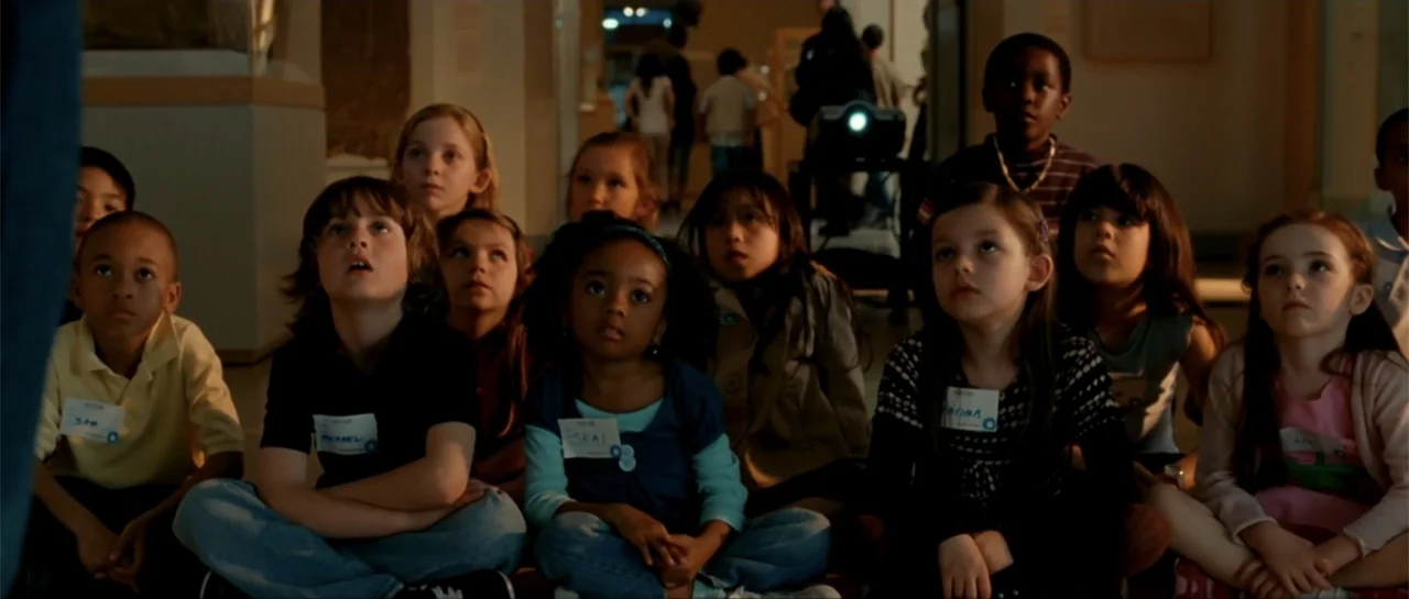 The Rebound (2009) movie still: medium — A dimly lit museum hall features a group of diverse children sitting on the floor. The children look…
