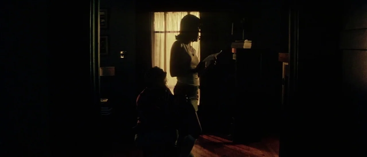 Pretty Persuasion (2005) movie still: medium — A dark, dimly lit room with a bright window visible in the background. A woman stands reading a paper…