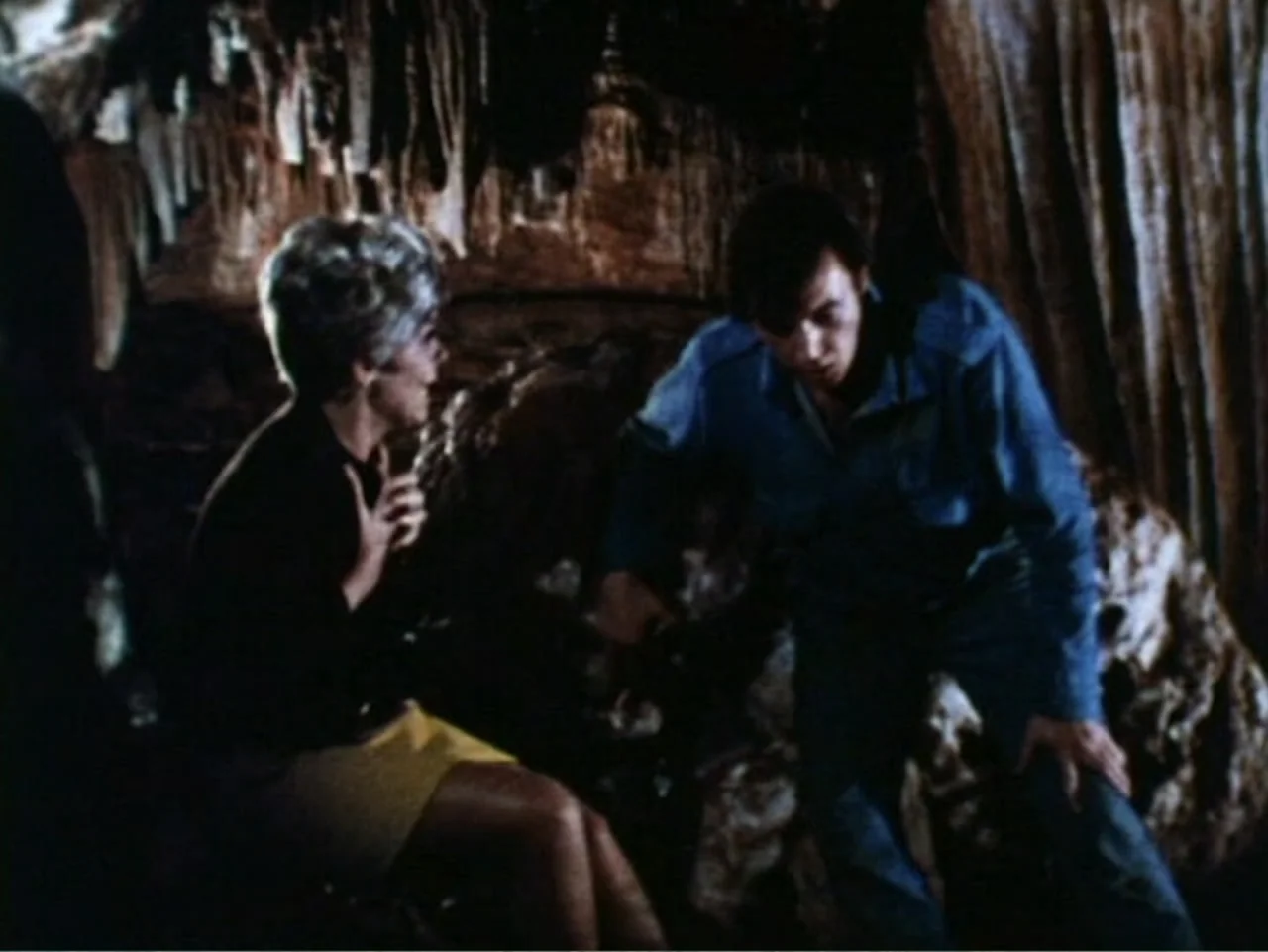 It's Alive (1974) movie still: medium — A dark subterranean cavern features jagged, textured rock walls and natural geological formations. A man in…