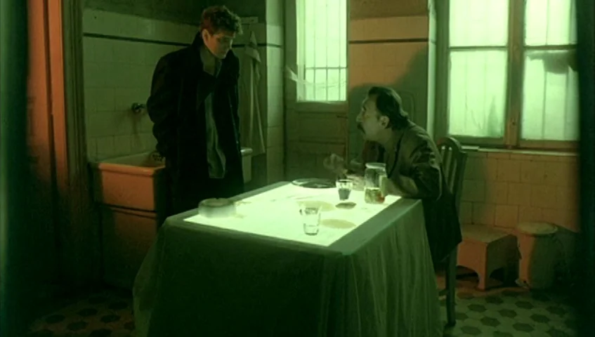 Almanac of Fall (1984) movie still: wide — A dilapidated, sterile room features tiled walls and a small table with papers. Two men interact in the…