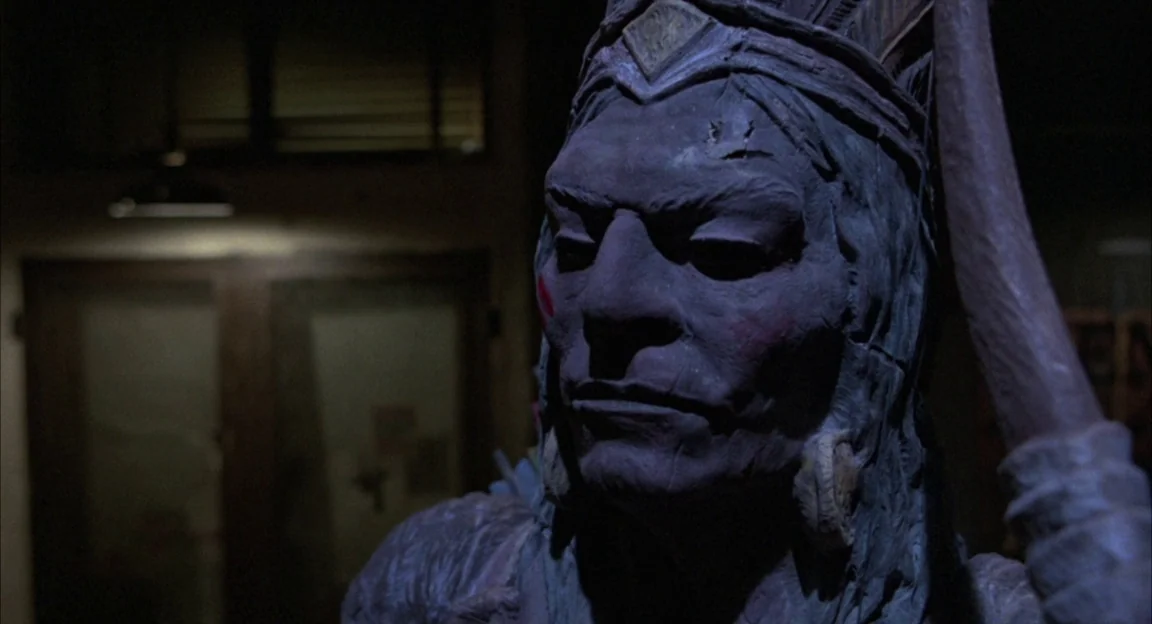 Creepshow 2 (1987) movie still: closeup — A wooden statue of a man stands inside a darkened room at night. The carving shows detailed facial…