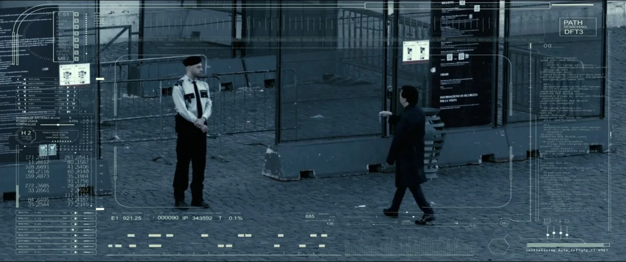 My Spy The Eternal City (2024) movie still: fullbody — A stone-paved public plaza features metal security barriers and informational signage. A…