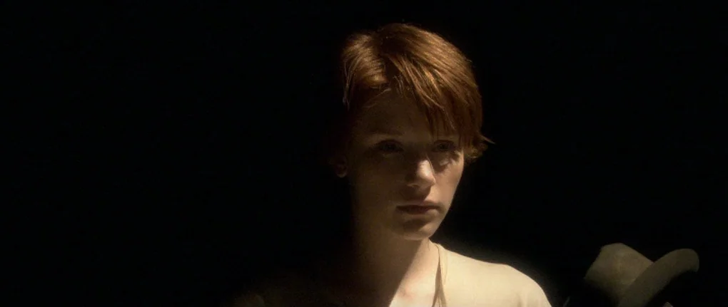 Manderlay (2005) movie still: closeup — A person stands in a completely dark environment with no visible background details. The individual gazes…