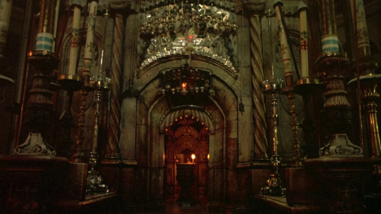 Powaqqatsi (1988) movie still: establishing — An ornate stone archway features complex carvings and gold-leaf details in a dimly lit space. Tall…
