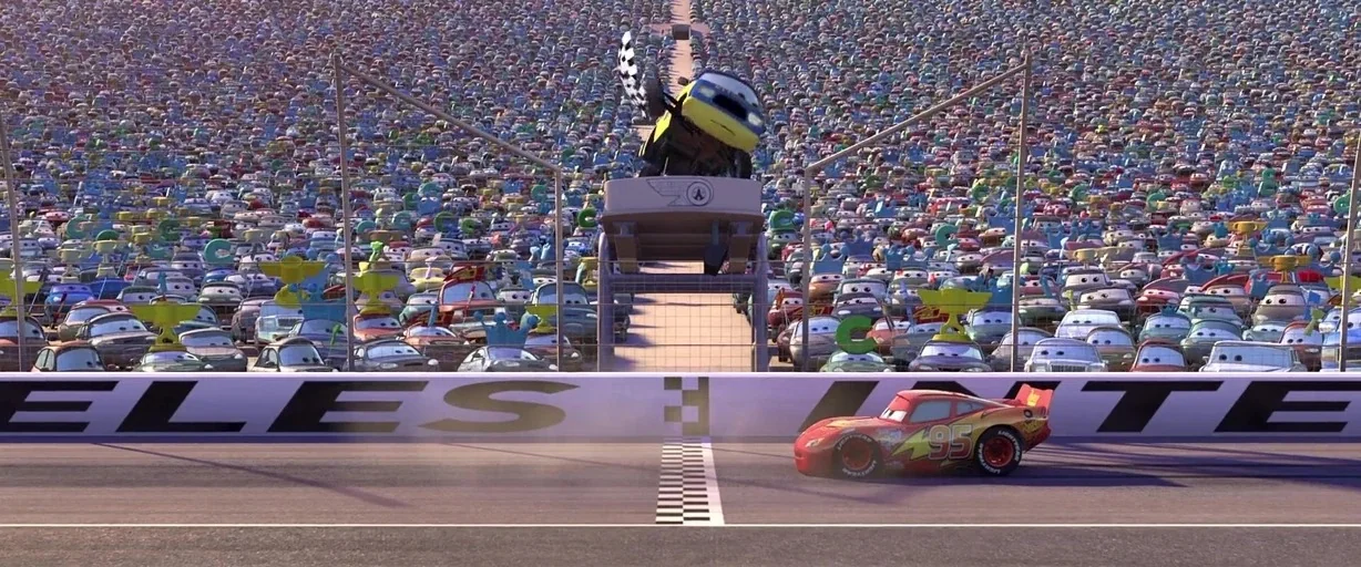 Cars (2006) movie still: wide — A vast crowd of automobiles fills the stadium seats behind a race track finish line. A red race car with number 95…