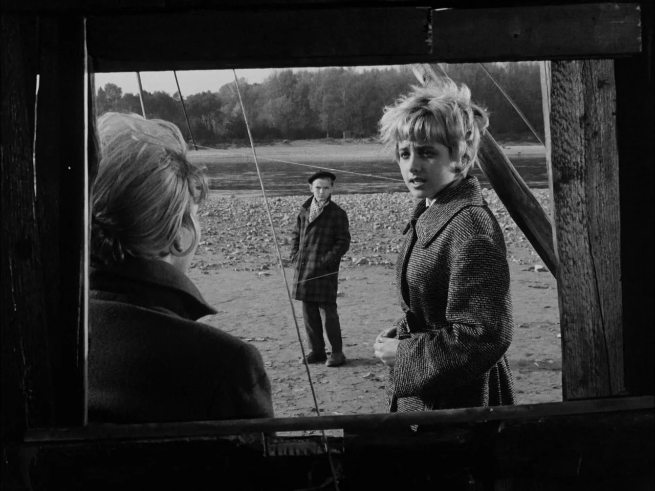 The Sun In A Net (1963) movie still: medium — A riverbank is framed by a rectangular wooden structure opening. Two young women converse while a boy…