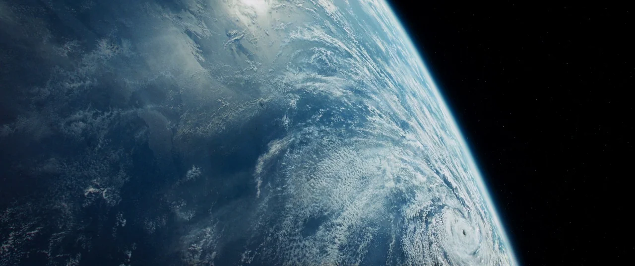 Gravity (2013) movie still: establishing — The curved horizon of Earth is visible against the deep black void of space. Dense white cloud systems…