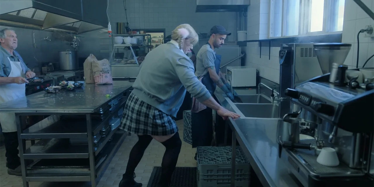 Ricky Stanicky (2024) movie still: fullbody — A stainless steel industrial workspace contains multiple work stations, sinks, and metal shelving…