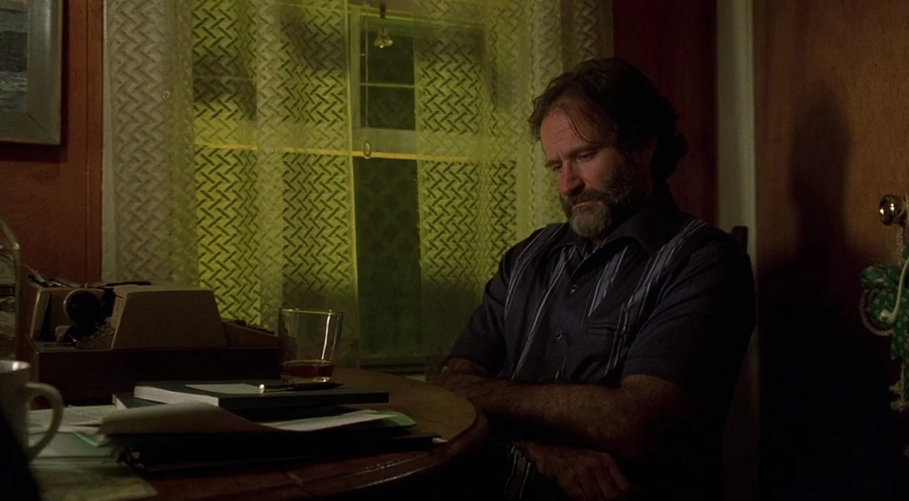 Good Will Hunting (1997) movie still: medium — A man sits at a round wooden table in a dimly lit room at night. Papers and a glass of liquor rest on…