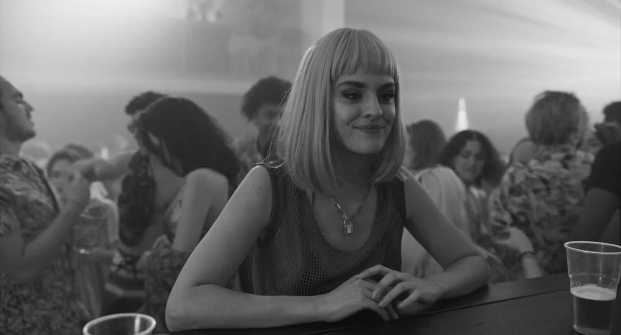 Paris, 13th District (2021) movie still: medium — A crowded nightclub bar area features blurred figures moving behind a central subject. A young…