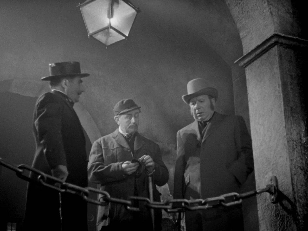 Le Plaisir (1952) movie still: medium — A dark, arched stone passage is illuminated by a single hanging lantern. Three men in period hats and coats…