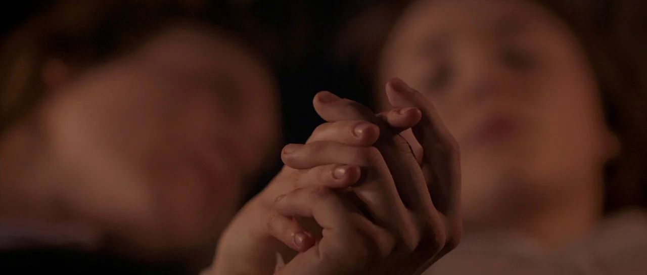 Byzantium (2012) movie still: closeup — Two people lie in a dark, out-of-focus bedroom. Their hands are held together in the center of the frame.