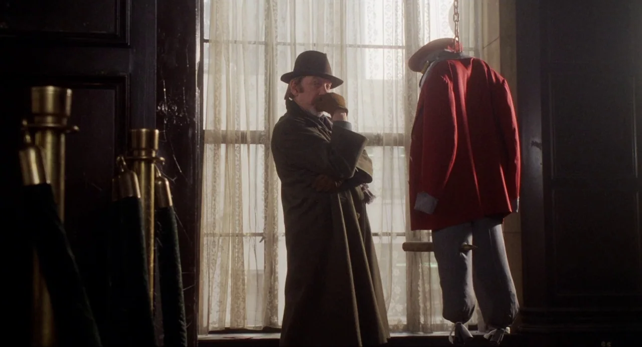 Buffy the Vampire Slayer (1992) movie still: medium — A dimly lit room with floor-to-ceiling windows covered by lace curtains. A man in a trench…