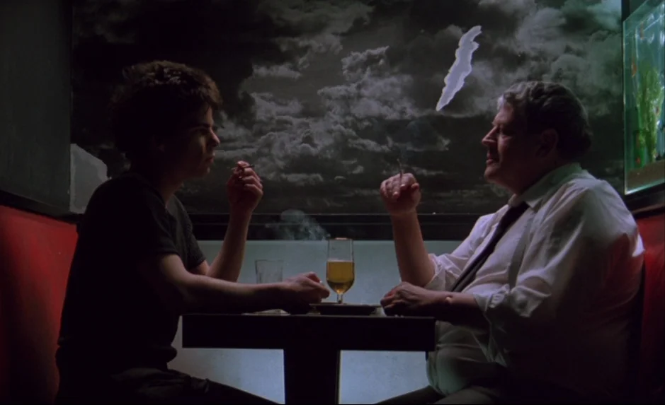 Mauvais Sang (Bad Blood) (The Night Is Young) (1986) movie still: medium — A diner booth with red vinyl seats sits before a mural of a dark sky. Two…