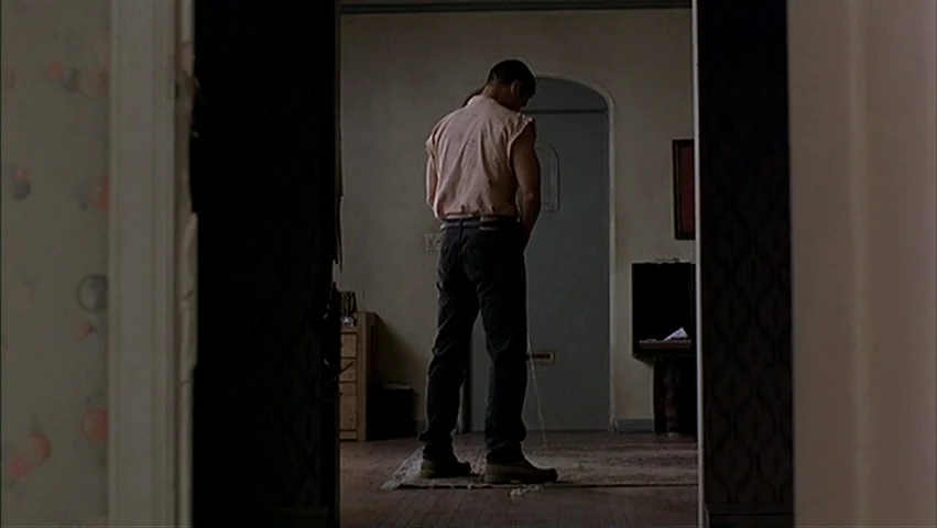 The Big Lebowski (1998) movie still: fullbody — A sparsely furnished room with muted walls and a central patterned area rug. A man stands in the…