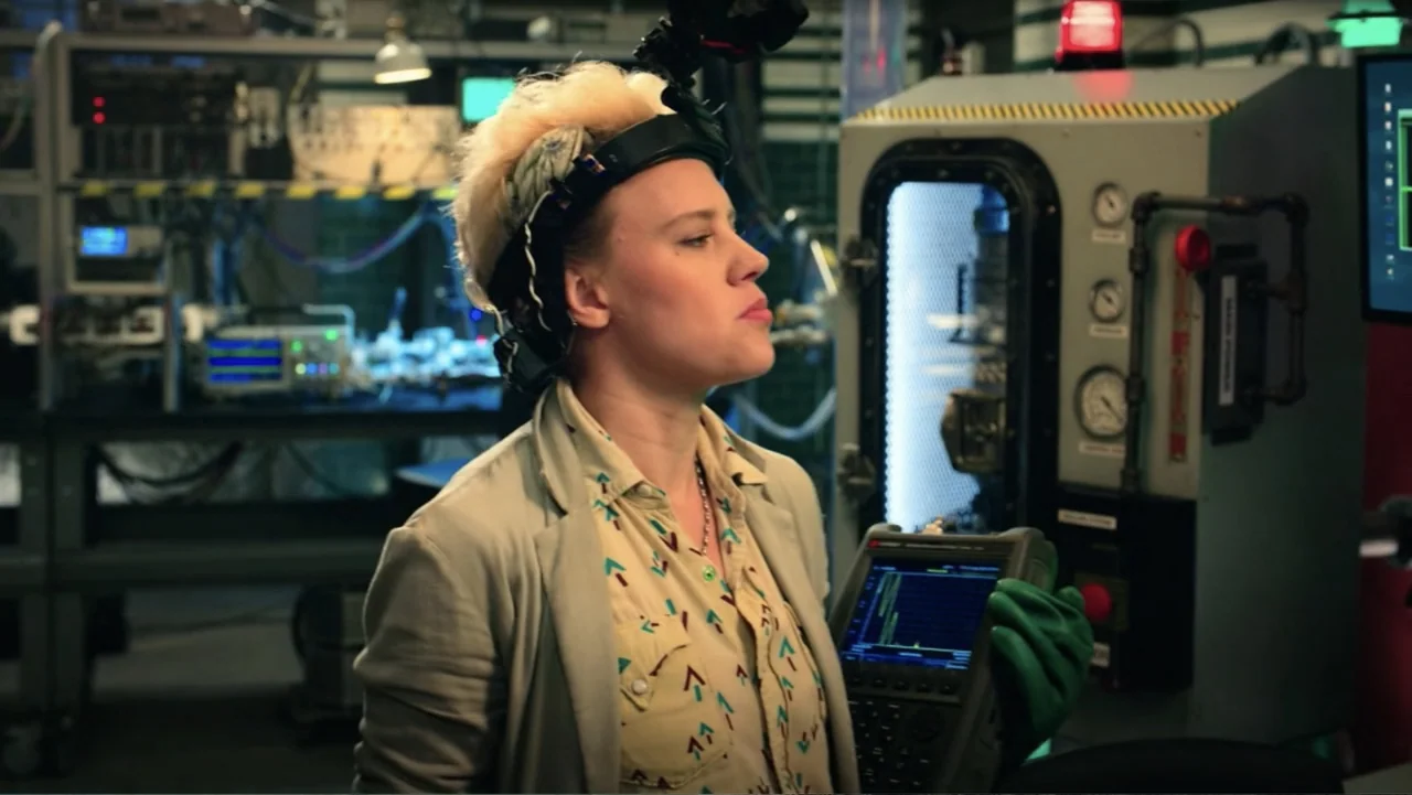 Ghostbusters (2016) movie still: medium — A cluttered laboratory environment featuring complex electronic machinery and industrial control panels. A…