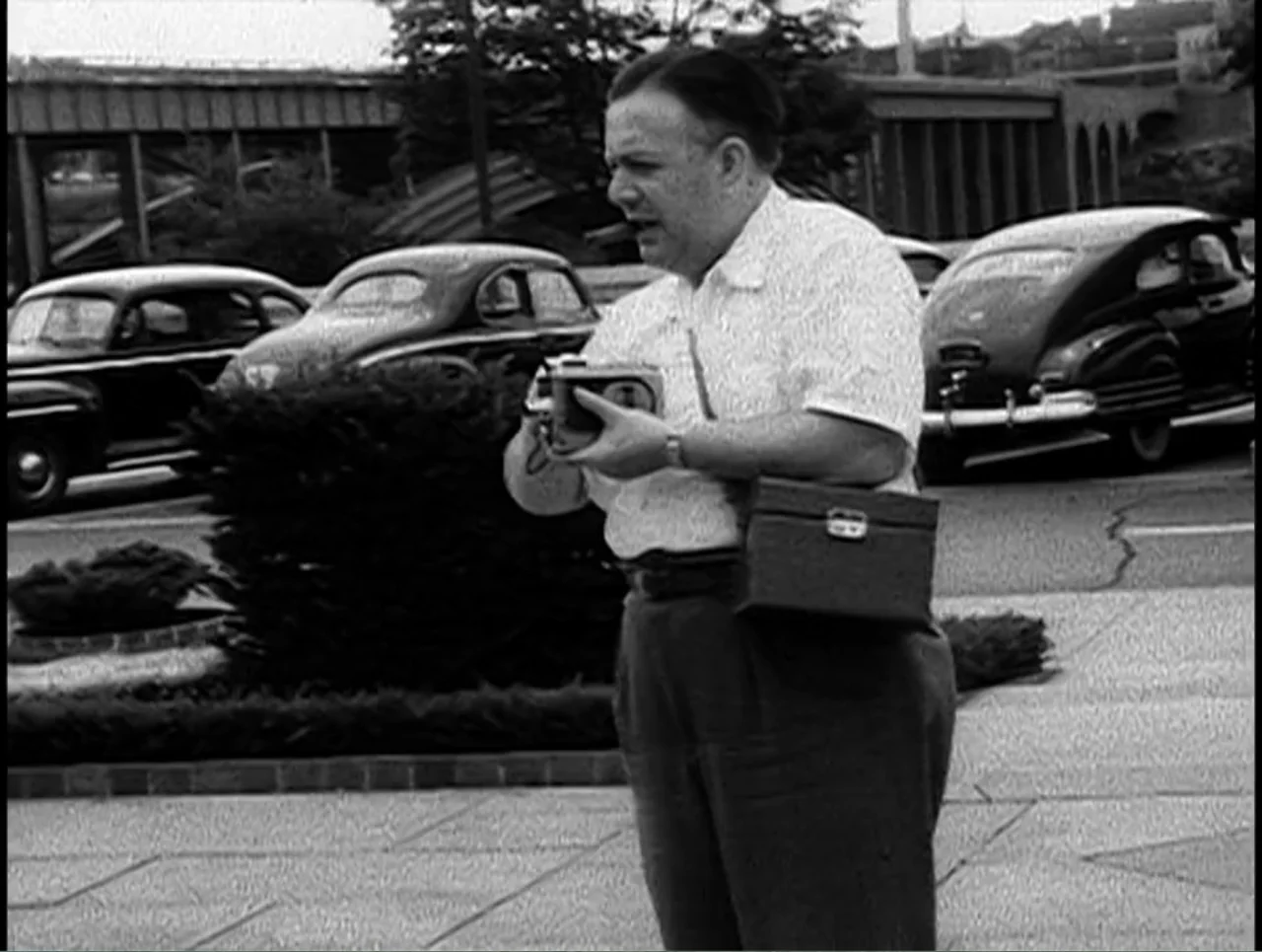 First Cousin Once Removed (2012) movie still: medium — A parking lot features parked vintage automobiles and a small hedge in the background. A man…