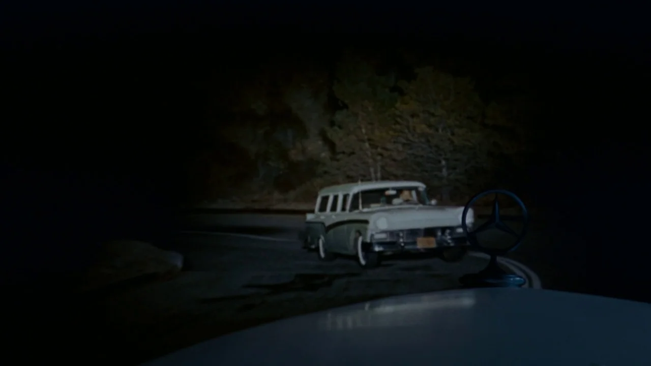 North By Northwest (1959) movie still: wide — A dark, winding road passes through a wooded area under the night sky. A vintage station wagon drives…