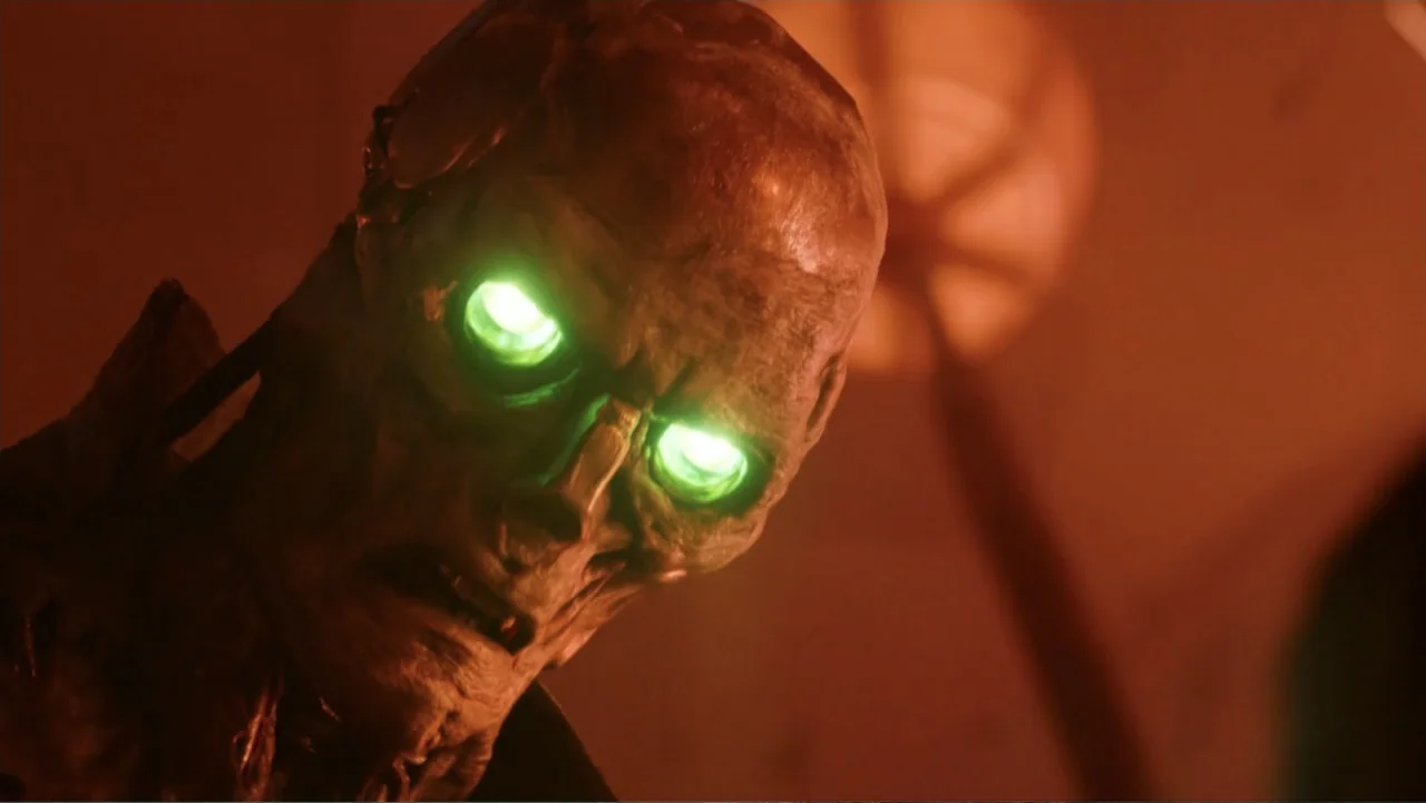 Mortal Engines (2018) movie still: closeup — A dark, dimly lit interior space contains a single humanoid figure. The subject has textured, leathery…
