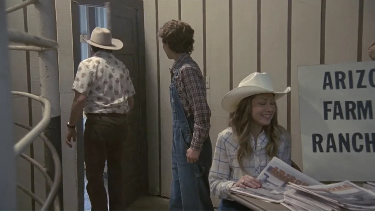 Temple Grandin (2010) movie still: medium — A utilitarian room features wood-paneled walls and a sign referencing a ranch business. A man walks…
