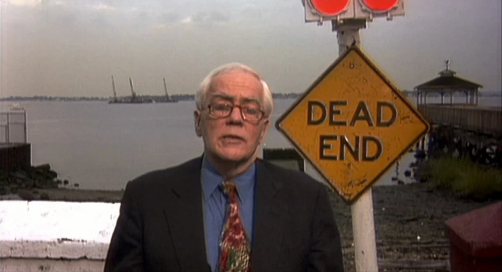 Summer of Sam (1999) movie still: medium — A man stands before a waterfront with a large diamond-shaped yellow warning sign. He speaks to the…