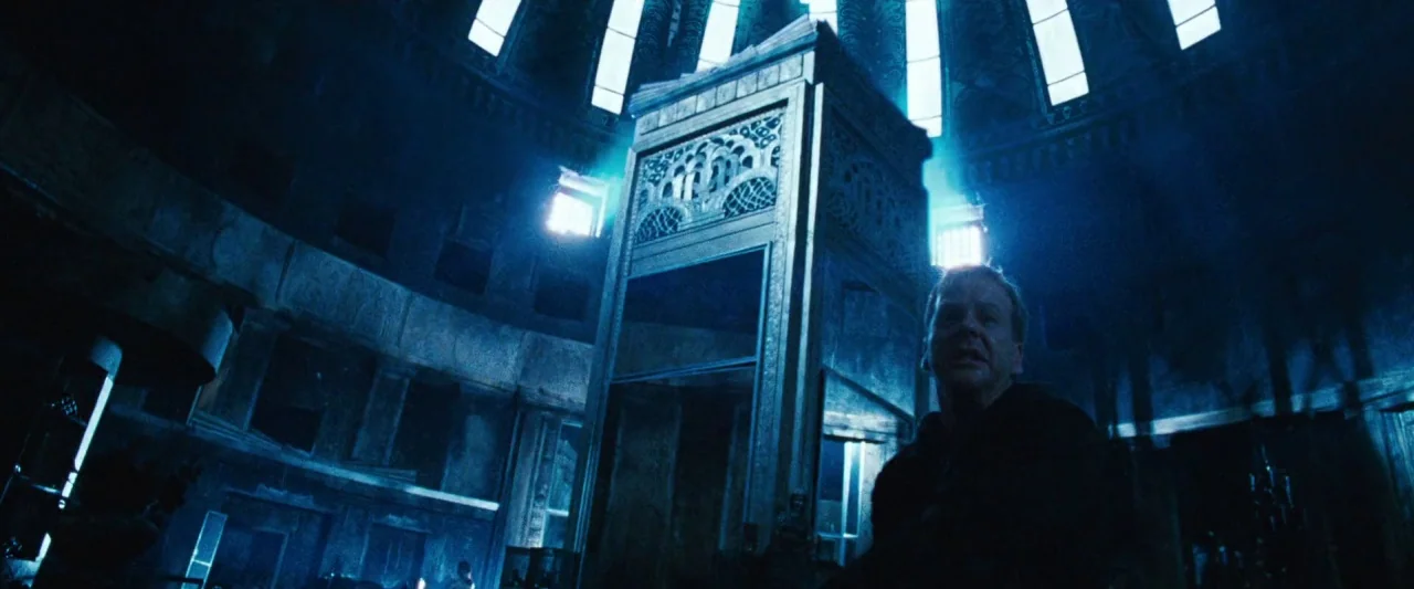 Mirrors (2008) movie still: medium — A dark vaulted room features a large central stone pillar and high arched windows. A man stands in the…