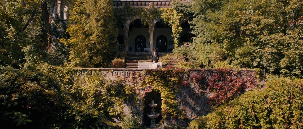 The Duke of Burgundy (2014) movie still: wide — A stone terrace overgrown with autumnal vines leads to a mansion with arched doorways. Two people…