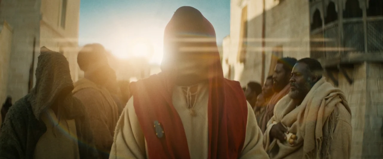 The Book of Clarence (2023) movie still: medium — An ancient stone street is lined with weathered buildings under bright daylight. A central figure…