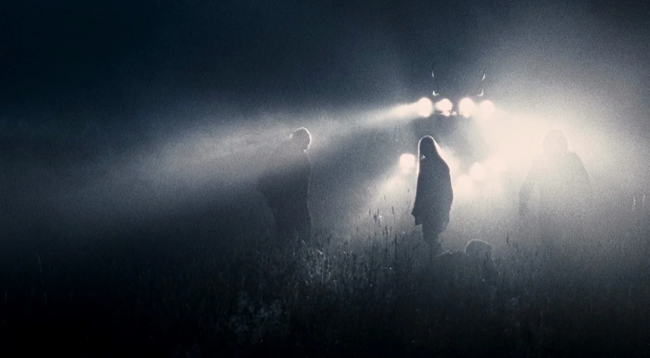 Halloween 2 (2009) movie still: wide — Three people stand in a field obscured by thick, glowing fog at night. Bright headlights from an approaching…
