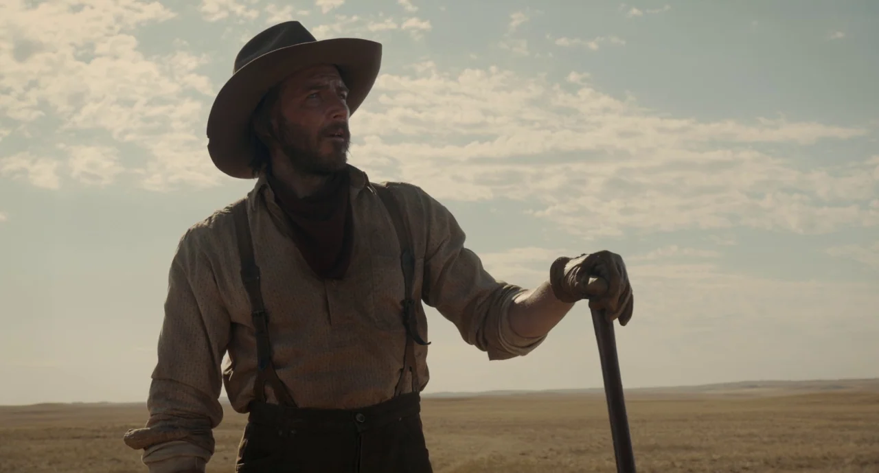 The Ballad of Buster Scruggs (2018) movie still: medium — An arid, grassy plain stretches out under a wide, cloudy sky in the American West. A man…