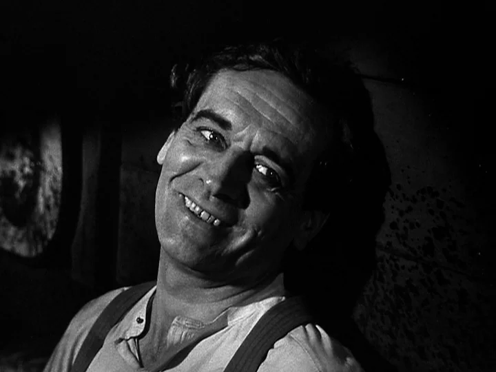 Nightmare Alley (1947) movie still: closeup — A dimly lit room with heavy shadows cast against a wall. A man stares forward with a smile.