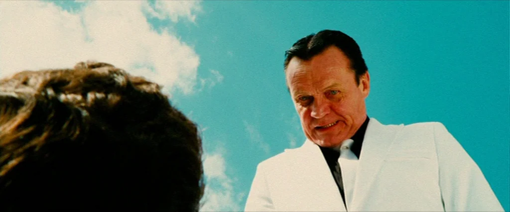 Hobo With A Shotgun (2011) movie still: medium — An elderly man in a white suit looms over someone under a bright sky. The camera perspective is…