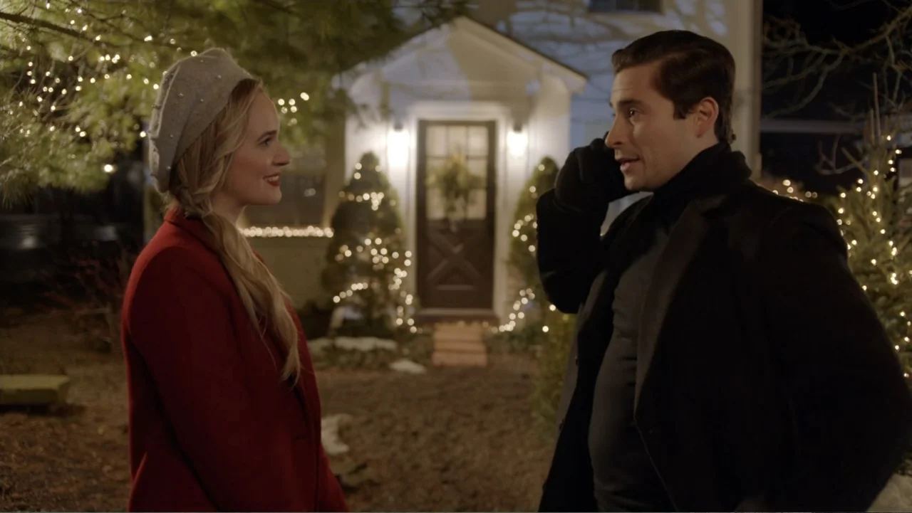 Loving Christmas (2022) movie still: medium — A residential front yard at night with string lights decorating several small pine trees. A woman in a…