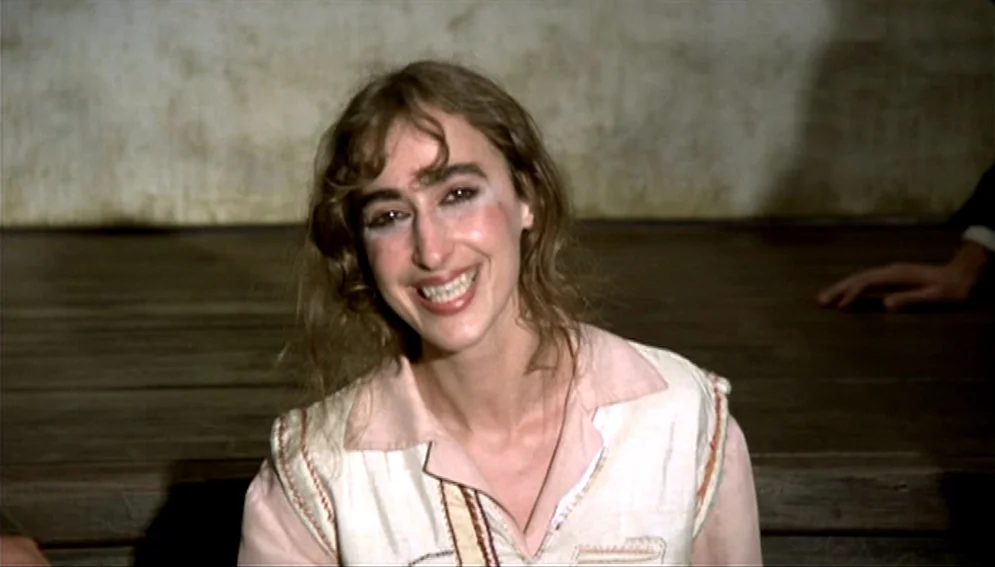 Orchestra Rehearsal (1978) movie still: closeup — A wooden performance surface sits before a plain, light-colored backdrop. A young woman with long…