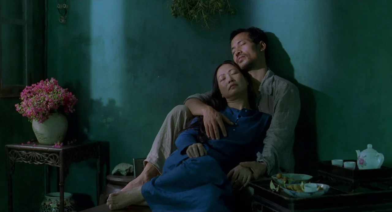 The Vertical Ray of the Sun (2000) movie still: medium — A green-walled interior features a couple resting together on the floor. A side table holds…