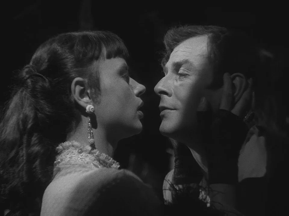 Sawdust and Tinsel (1953) movie still: closeup — A dark environment where two figures stand in sharp focus against a pitch-black background. A woman…