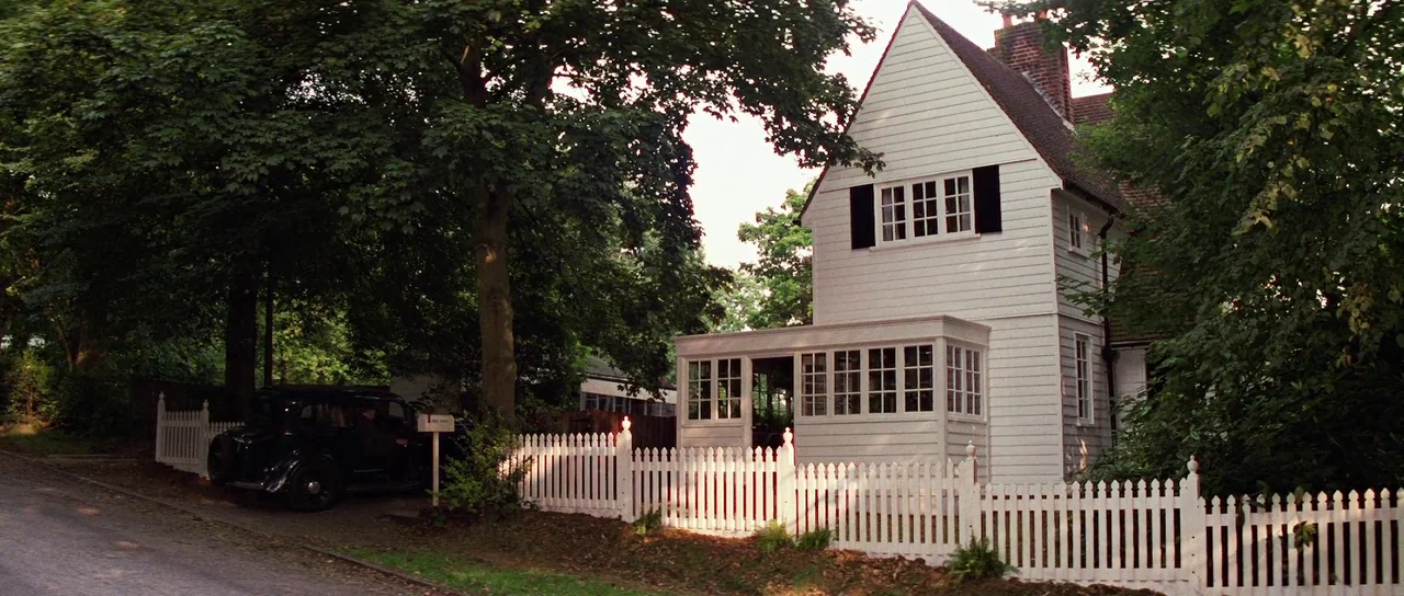 Indiana Jones and the Last Crusade (1989) movie still: wide — A white timber-sided house sits behind a white picket fence on a quiet road. Mature…